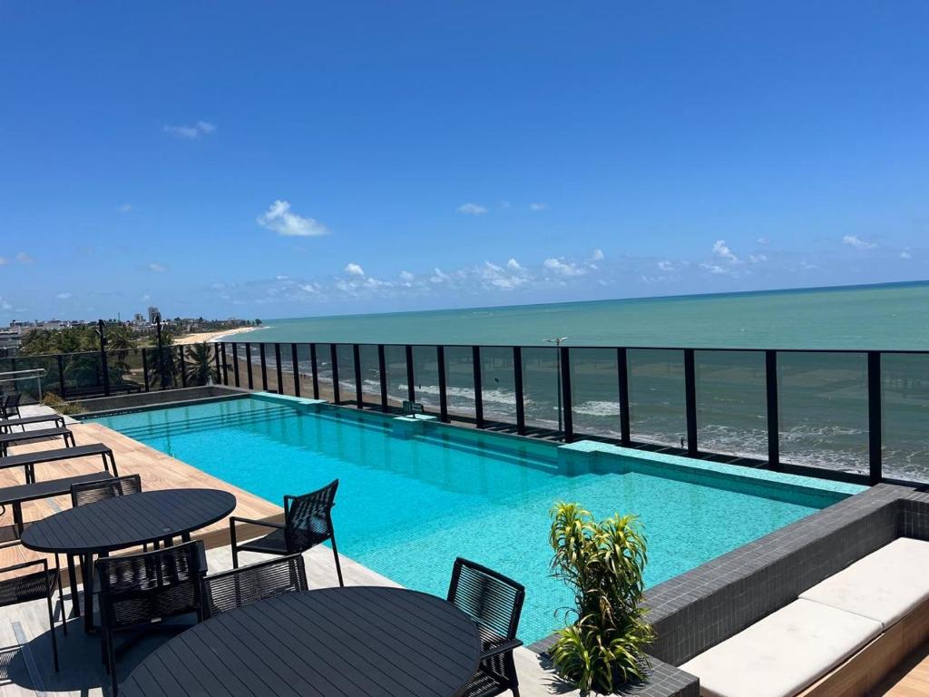 a swimming pool with tables and chairs and the ocean at Beach Haus beira mar bessa in Tambaú
