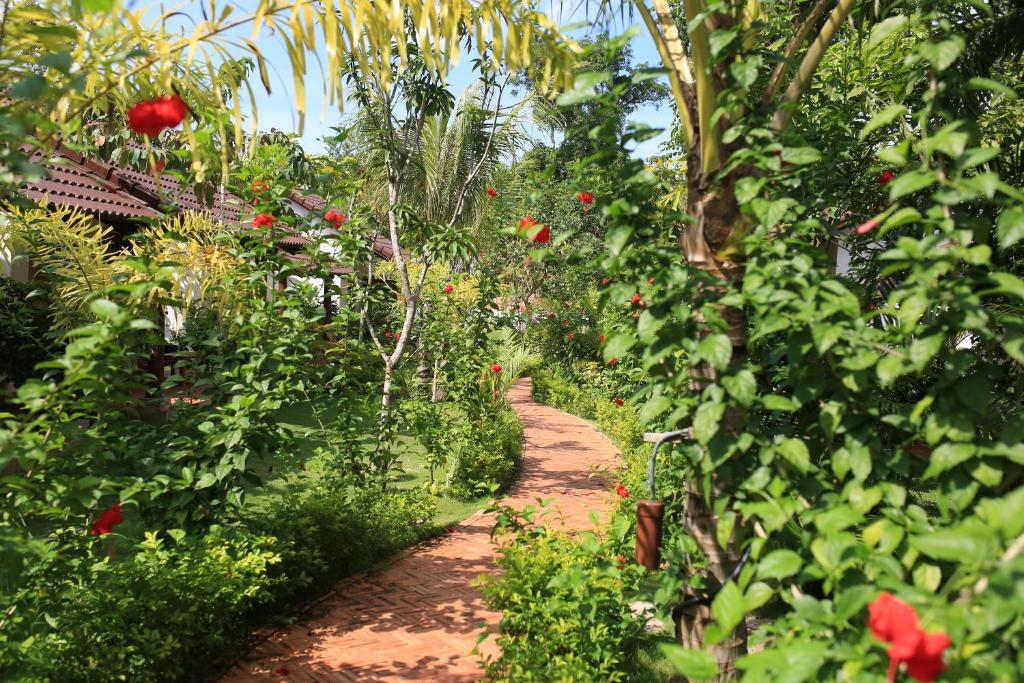 a path through a garden with red flowers and trees at La Mer Resort, Phú Quốc in Phú Quốc