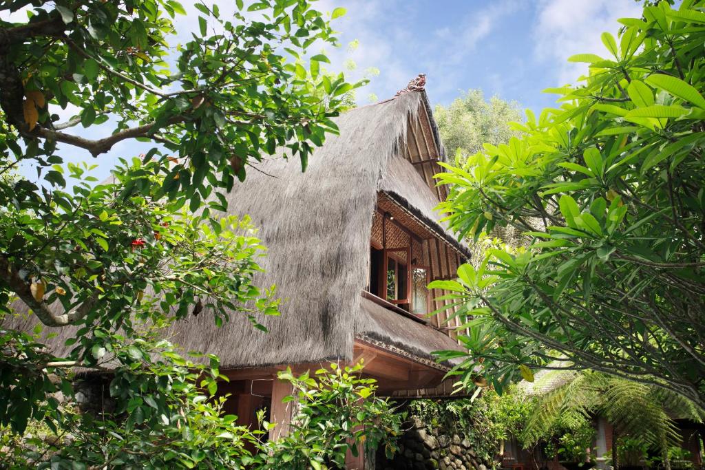 uma casa antiga com telhado de palha e árvores em Omah Pakem em Pakem