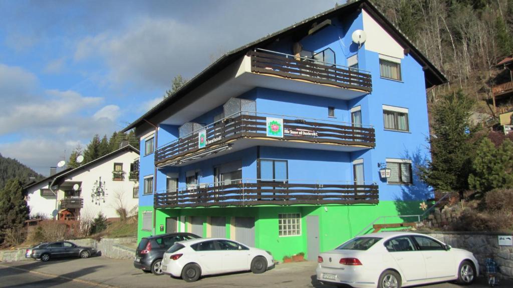 ein blaues und grünes Gebäude mit zwei Autos, die vorne geparkt sind in der Unterkunft Pension Blaues Haus in St. Blasien