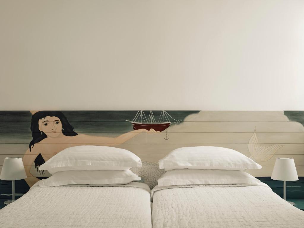 a room with three beds and a mural of a woman holding a boat at Acteon Hotel in Ios Chora