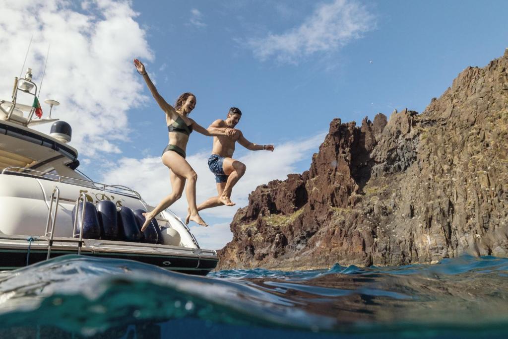 two people jumping off of a boat in the water at Dreams Madeira Resort Spa & Marina in Caniçal