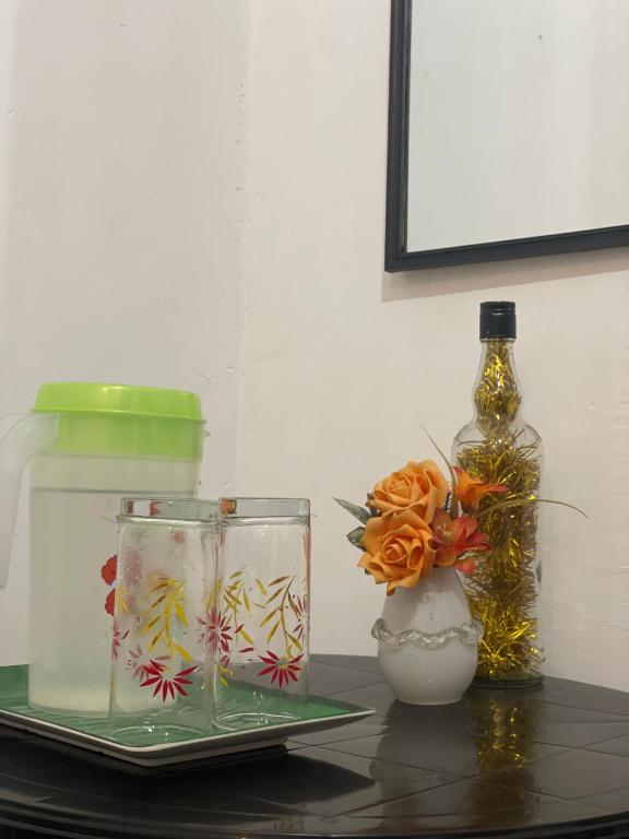 a table with a bottle and two glasses and a vase at Suriya Haven Homestay in Badulla