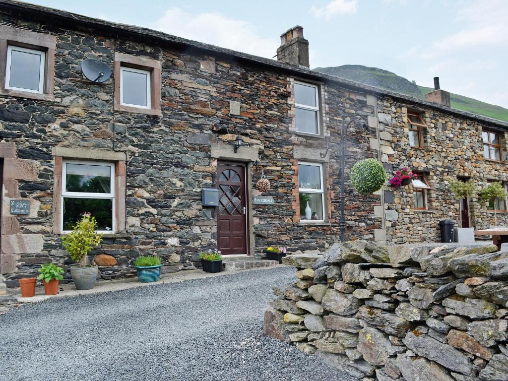 a stone house with a stone wall and a door at Brackendale Cottage - Uk1335 in Threlkeld