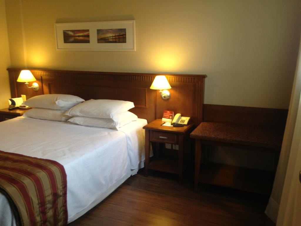 a hotel room with a bed and a table with a phone at Flat Gramado Alpen in Gramado