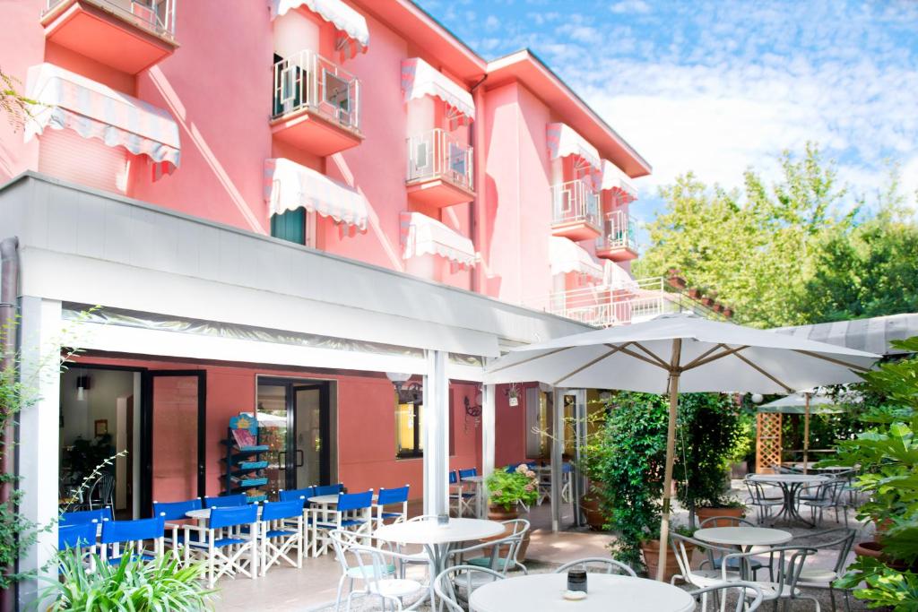 eine Außenterrasse eines rosafarbenen Gebäudes mit Tischen und Sonnenschirmen in der Unterkunft Hotel Villa Rosa in Cesenatico