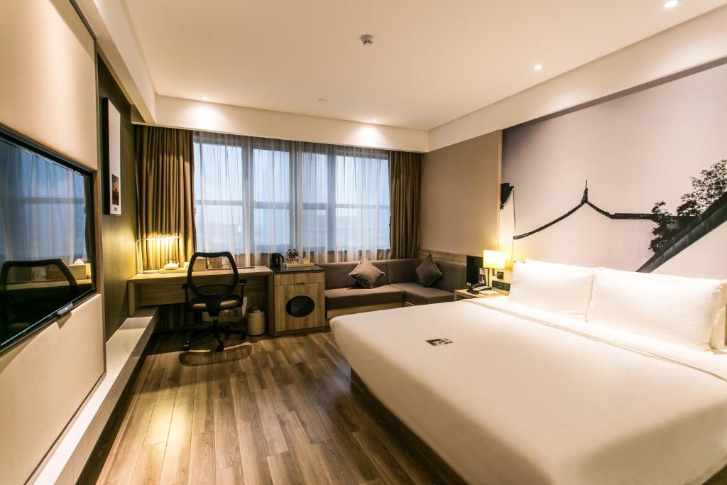 Atour Hotel Suzhou Jinji Lake Expo Center في سوتشو: غرفة فندقية بها سرير كبير ومكتب