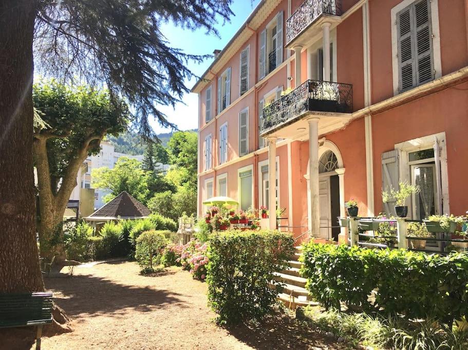 un bâtiment rose avec une terrasse couverte et un balcon dans l'établissement Grand T2 lumineux rénové Lamalou centre, à Lamalou-les-Bains