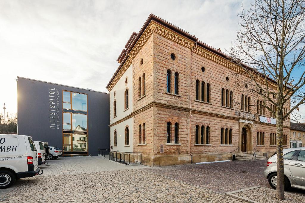 un gran edificio de ladrillo con coches aparcados en un aparcamiento en OX Hotel Altes Spital, en Müllheim