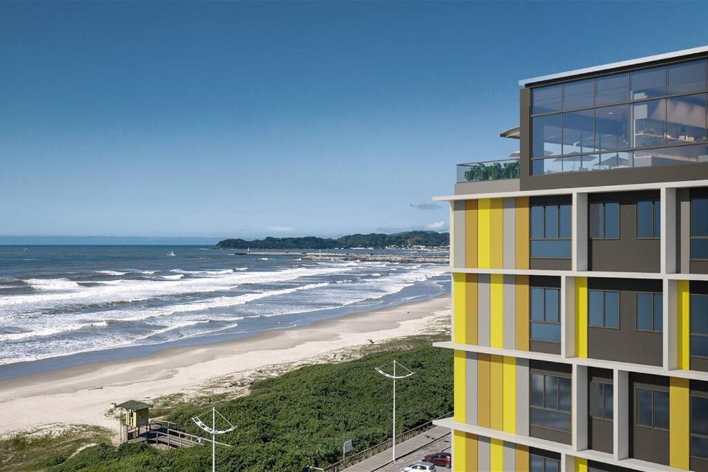 a yellow building next to a beach with the ocean at Apartamento beira mar in Navegantes