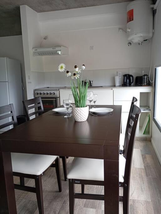 a dining room table with chairs and a table with flowers on it at Eneas Flat luminoso con cochera in Pinamar