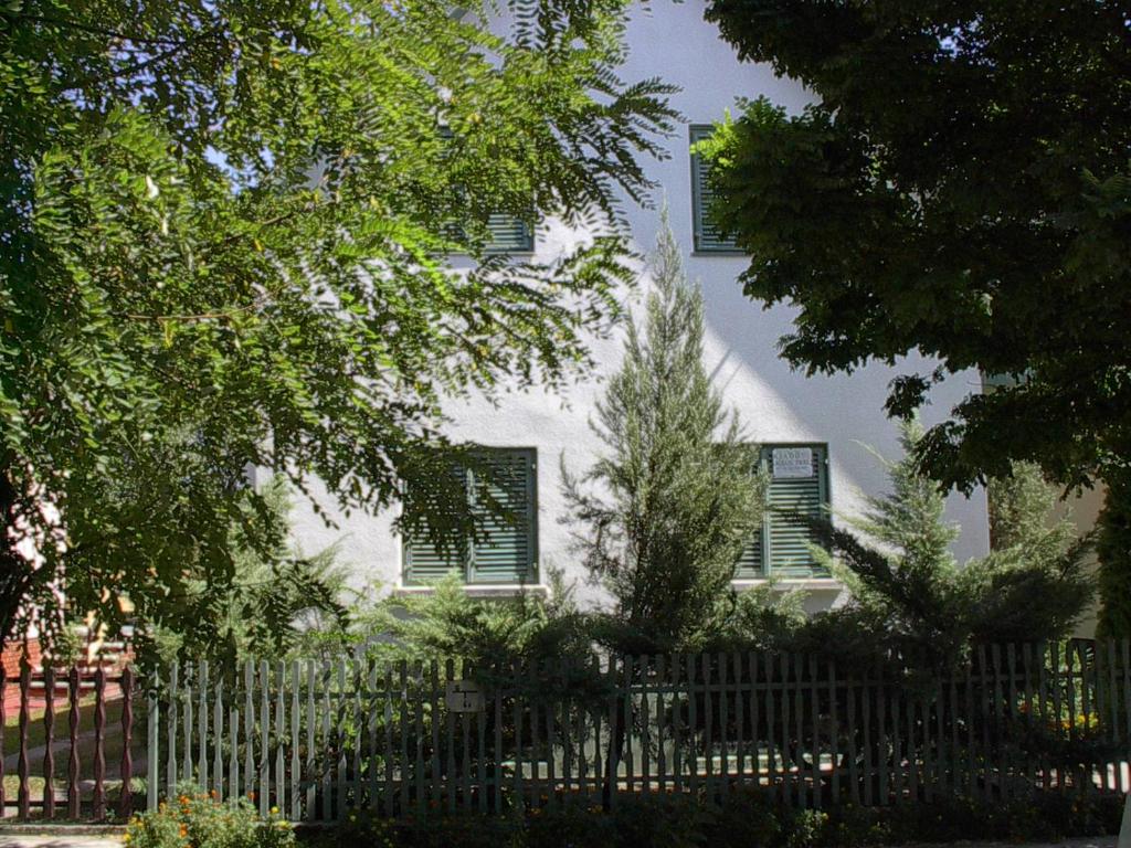 a white house with a fence and trees at Babarczi Üdülőház in Kiskunmajsa