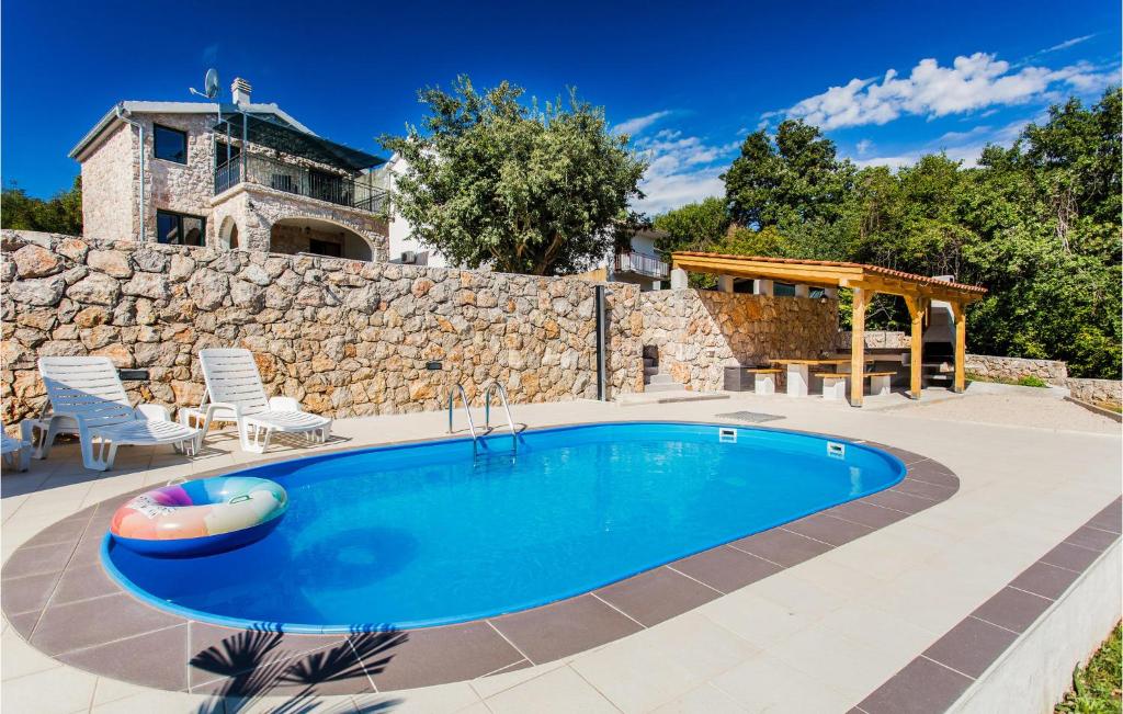 a swimming pool in front of a stone wall and a house at Awesome Home In Krk With Wifi in Risika