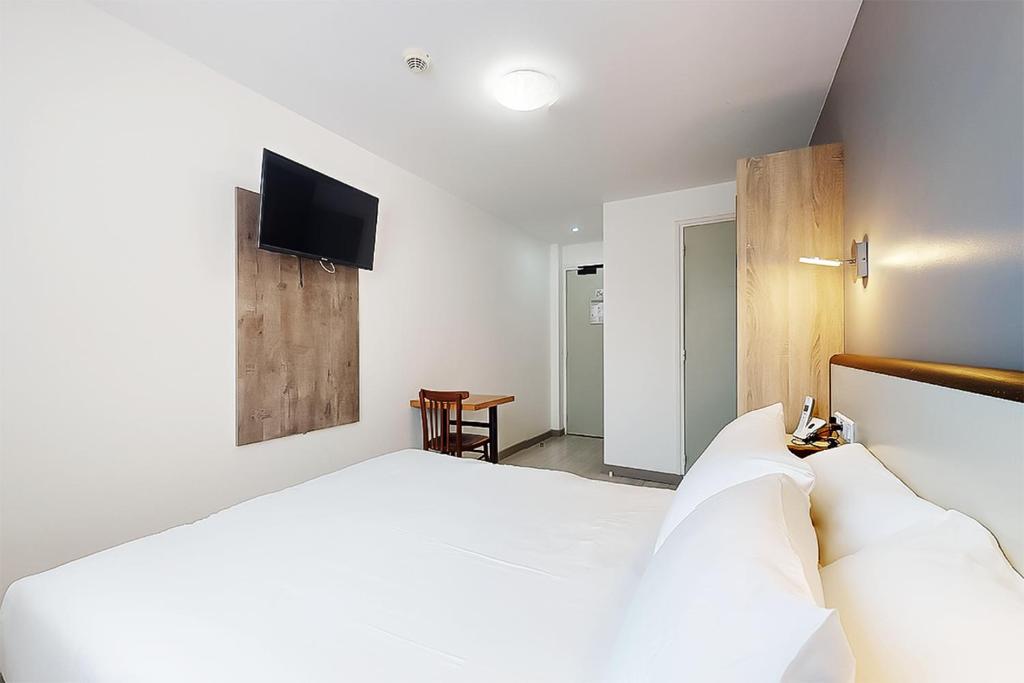 a bedroom with a white bed and a tv on the wall at Hôtel de Ménilmontant in Paris