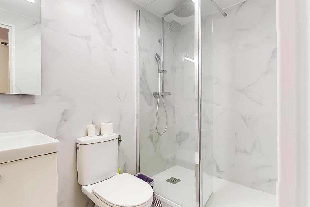 a white bathroom with a toilet and a shower at Hôtel de Ménilmontant in Paris