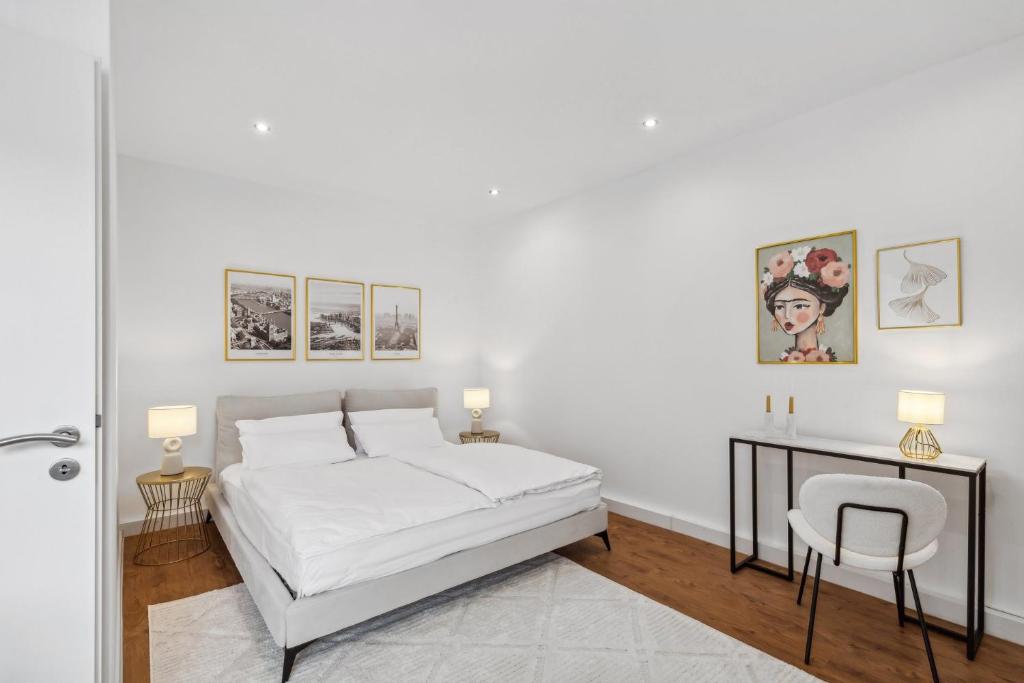 a white bedroom with a bed and a table and a chair at STARLIVING Premium Home in Osthofen