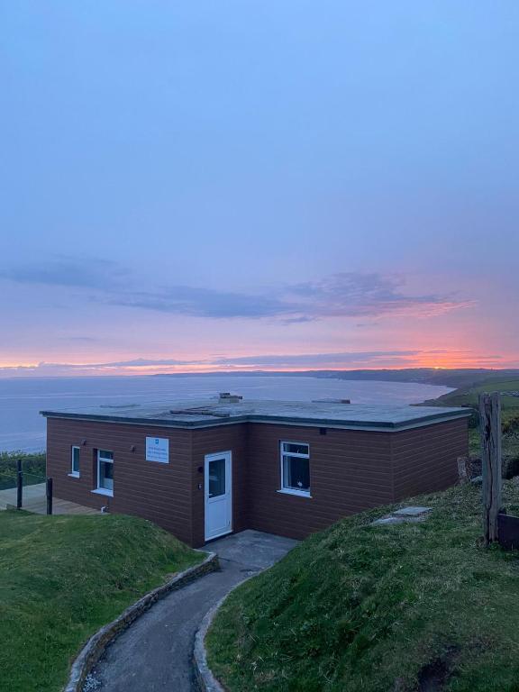 a small house on a hill with the sunset in the background at Sunset sea view chalet with hot tub in Torpoint