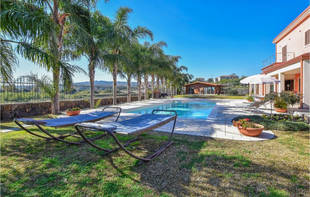 a pool with a bench and palm trees next to a house at 2 Bedroom Beautiful Home In Acireale in Acireale