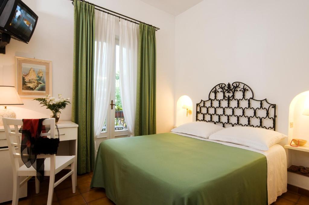 a bedroom with a green bed and a desk and a window at Hotel Villa Angelica in Ischia