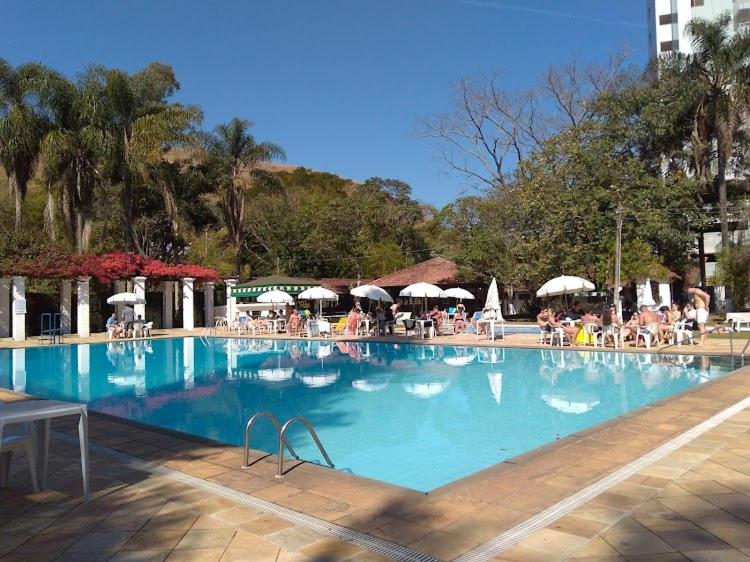 a large swimming pool with people sitting under umbrellas at Lindo studio no Residencial Quisisana in Poços de Caldas