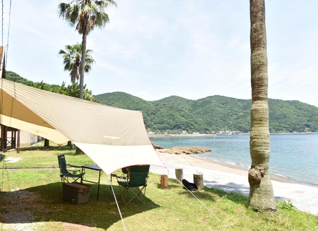 una tienda en la playa junto a una palmera en コテージ上浦, en Azamui