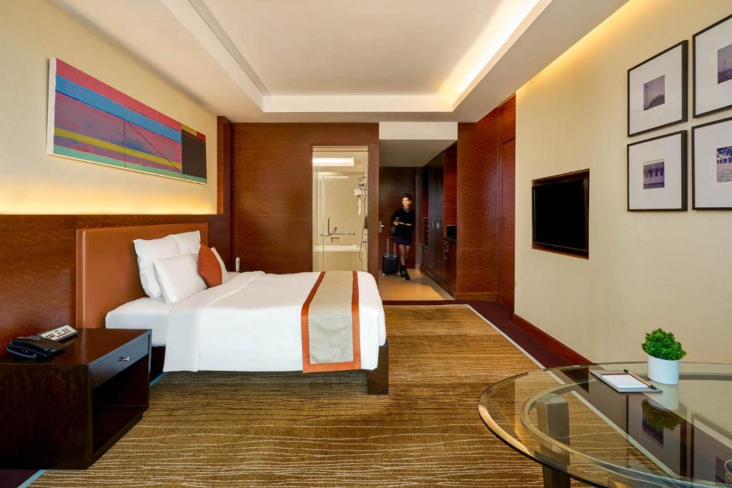 A modern guest room with a single bed, work desk, glass table, and bathroom entry.