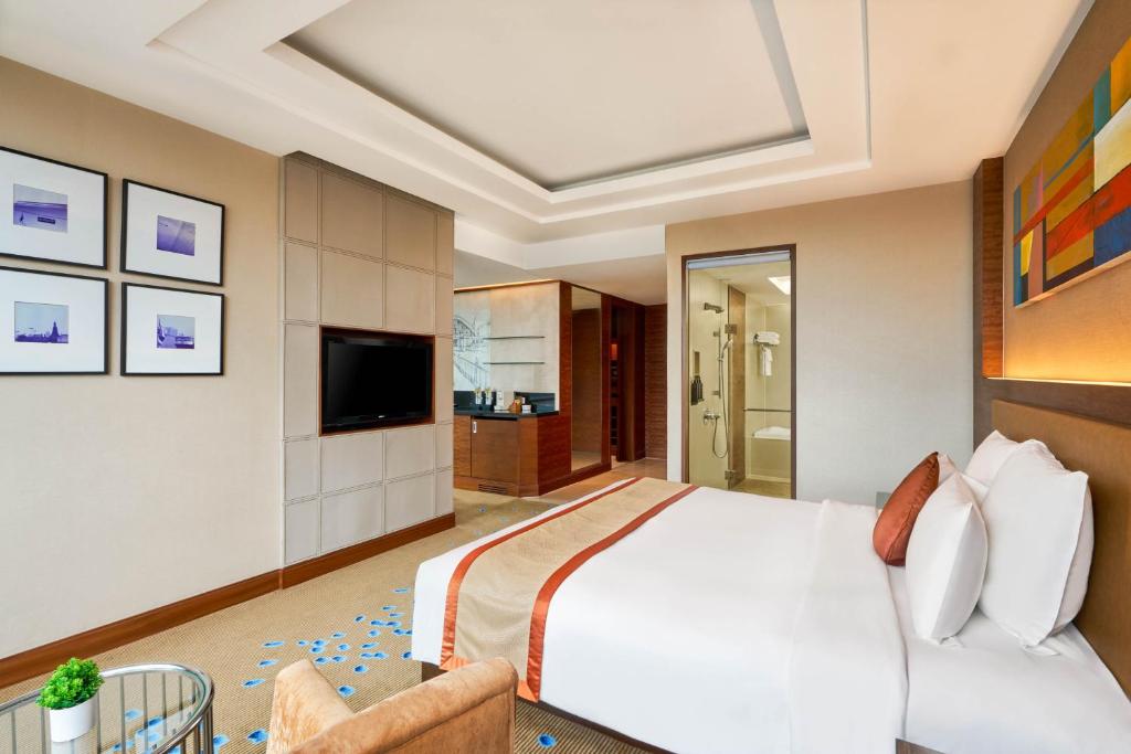 A spacious bedroom with a wall-mounted TV and a visible glass shower area.