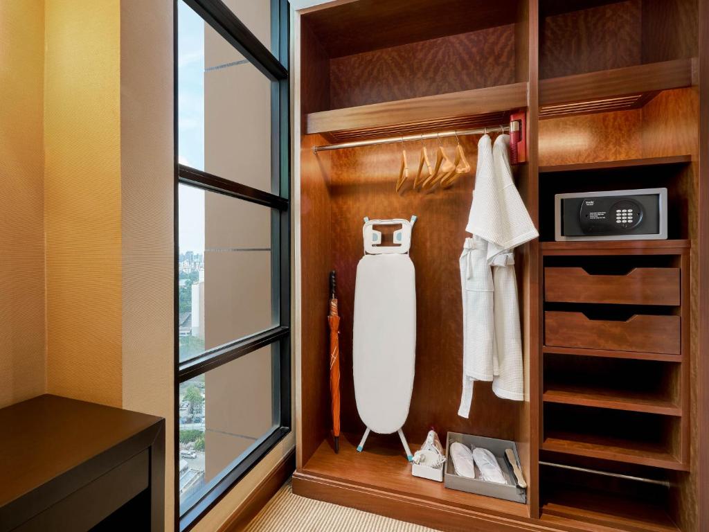 An open wooden wardrobe beside a tall window, with packing and garment-care amenities.