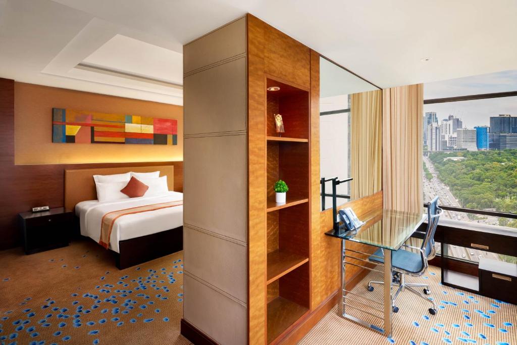 A bedroom with a glass-topped desk beside a large city-facing window.