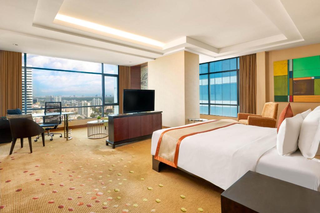 A corner bedroom with expansive windows, a desk and an urban panorama.