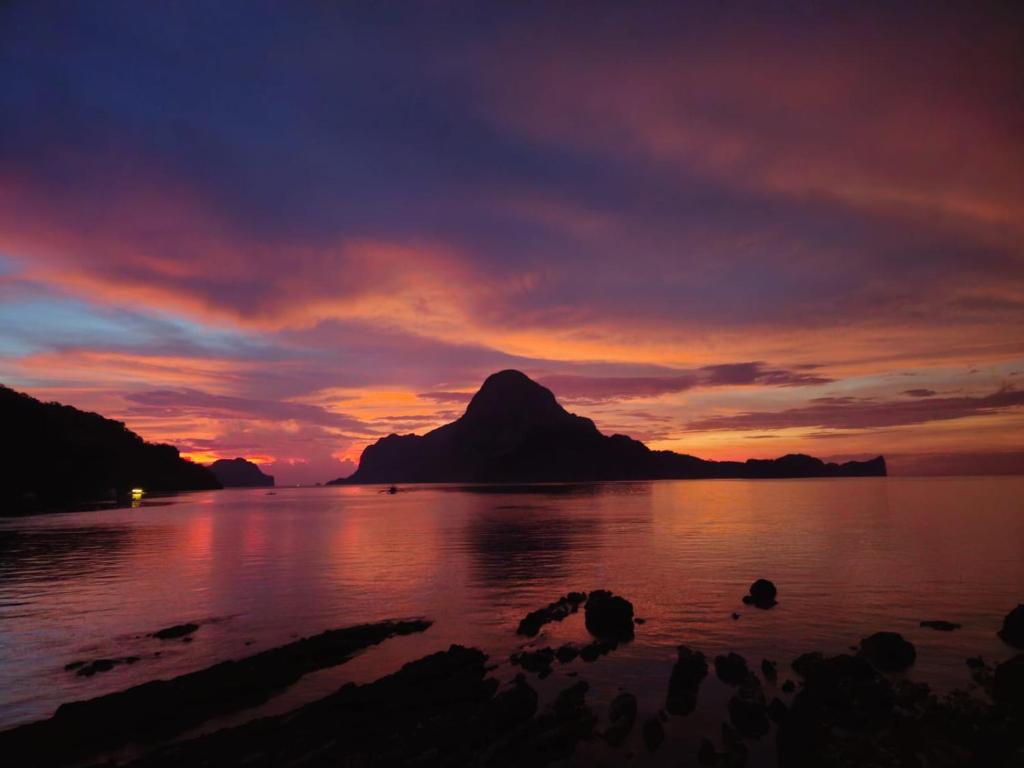 a sunset over a body of water with a mountain at Golden Monkey Beach Hotel in El Nido
