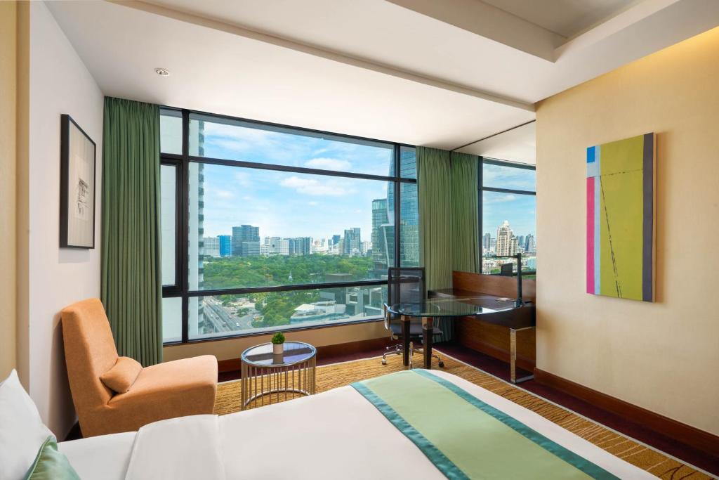 A bedroom corner with an armchair, small table, work desk and wide green-framed windows.