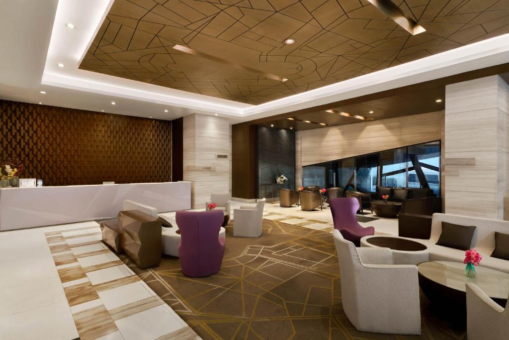 A warmly lit lobby lounge with varied seating, patterned carpet, and a long reception desk.