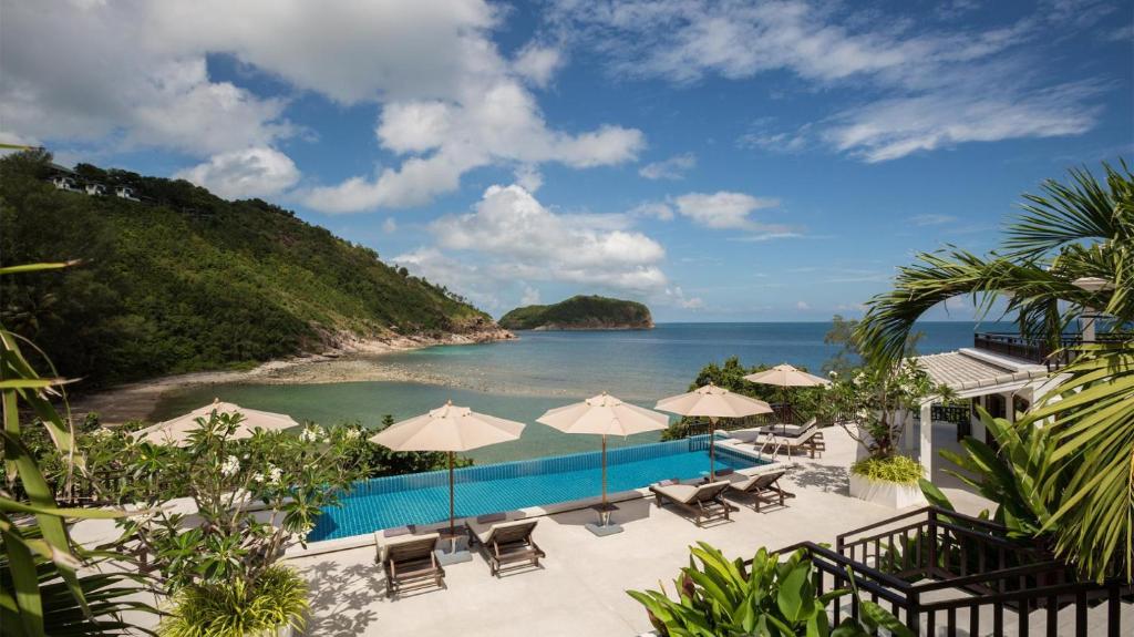 a pool with umbrellas and chairs and the ocean at The Secret Beach Villa in Mae Haad