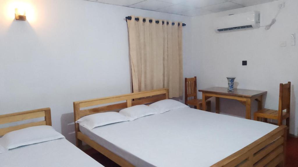 a bedroom with two beds and a table and a window at Anuhas Family Resort & Water House in Anuradhapura