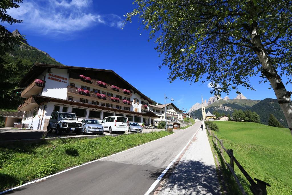 a street in a village with cars parked on the road at Albergo Arnica in Canazei