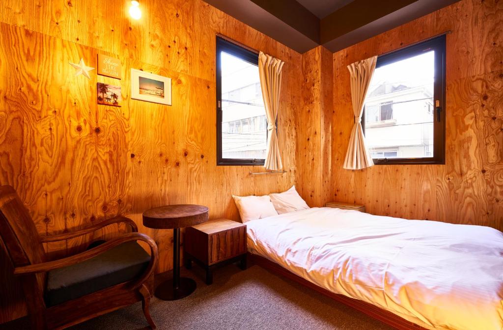 a bedroom with a bed and a chair and two windows at Focus Kuramae in Tokyo