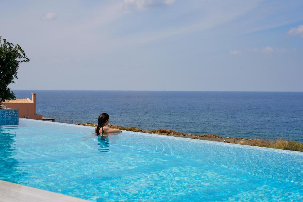 a woman sitting in a swimming pool looking at the ocean at Thalassa Residence, Heated Pool, Hot Tub & SeaView in Panormos Rethymno