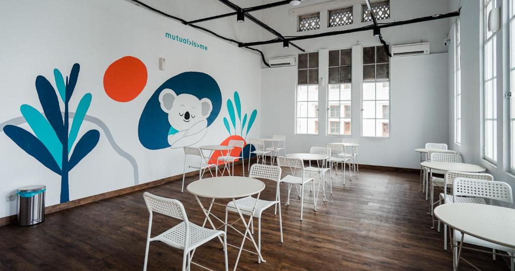 a room with tables and chairs in front of a mural at Bobopod Kota Tua, Jakarta in Jakarta