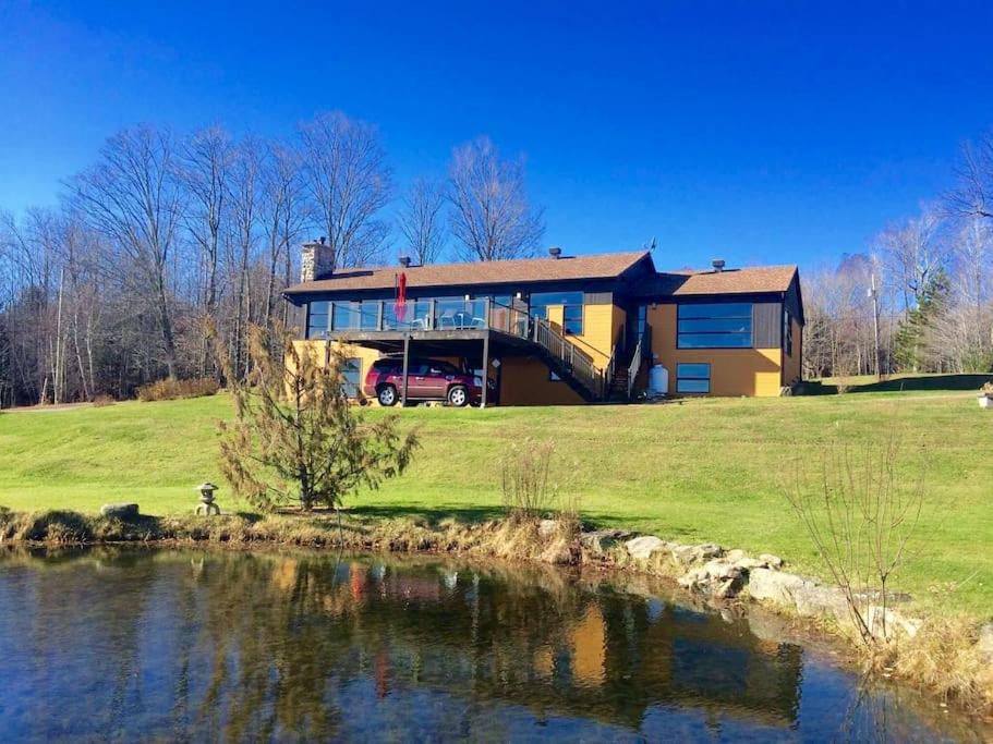 a house on a hill next to a body of water at Spacious luxurious Villa, bright cottage, pool, Jacuzzi, sauna, nature in Mansonville