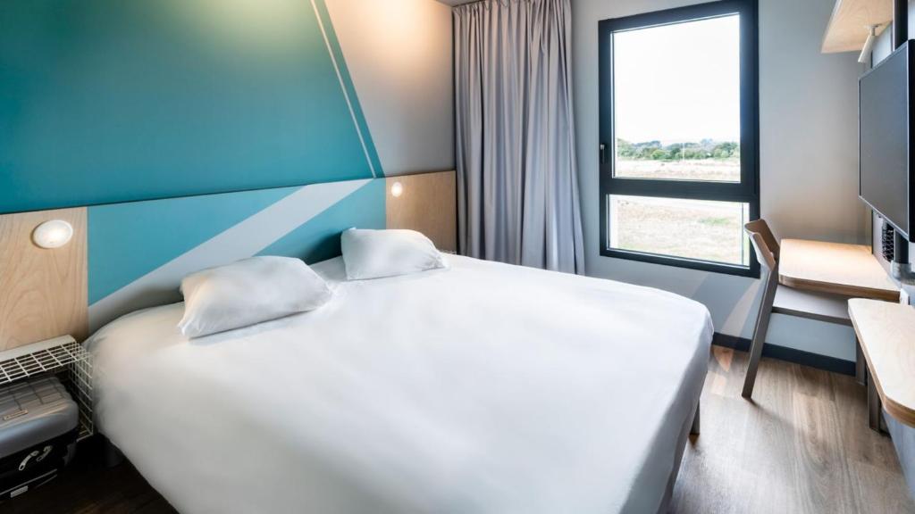 een hotelkamer met een groot wit bed en een raam bij ibis budget Morlaix in Morlaix
