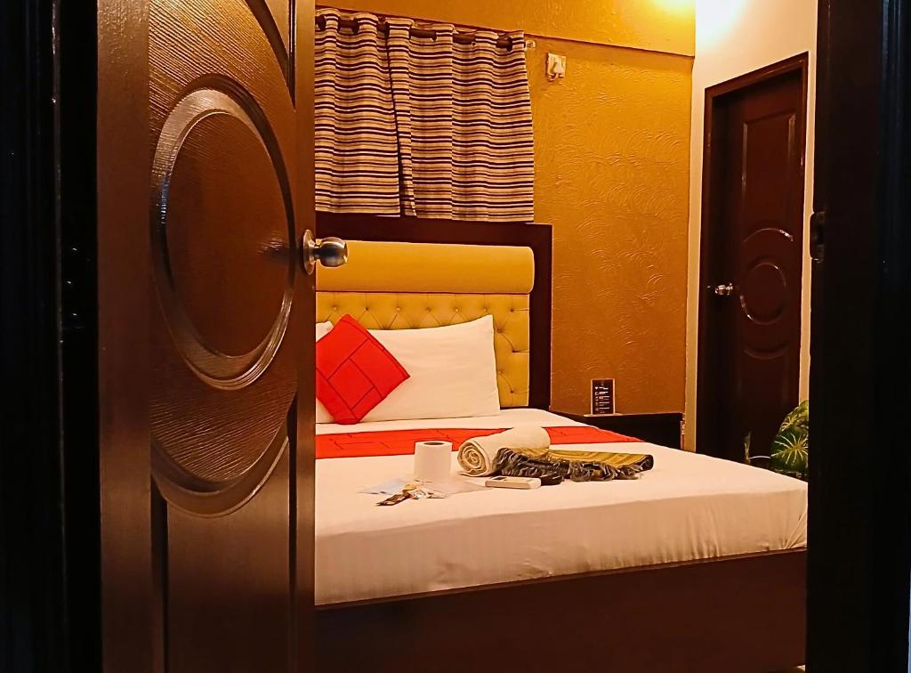 a bedroom with a bed with white sheets and red pillows at Hometown Apartments & Rooms in Karachi