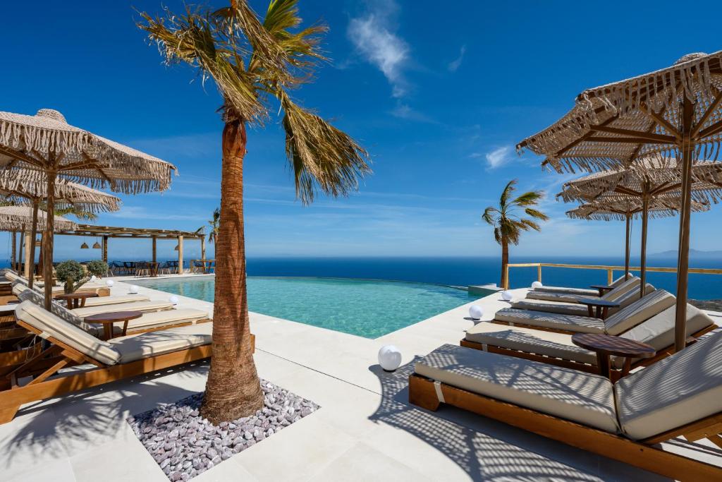 a resort infinity pool with chaise lounge chairs and a palm tree at Leon Luxury Suites in Imerovigli
