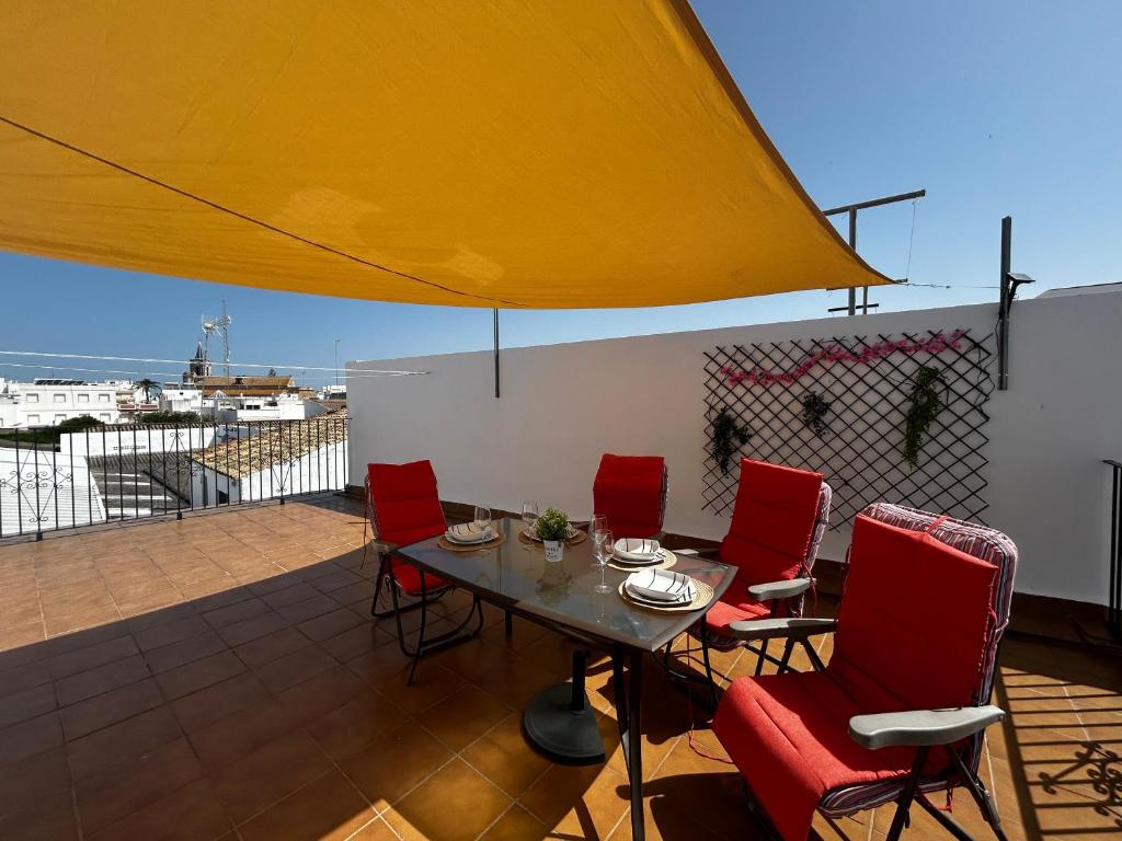 Un patio con sillas rojas y una mesa en un tejado. en Apartamento Beach&Relax Chipiona, en Chipiona