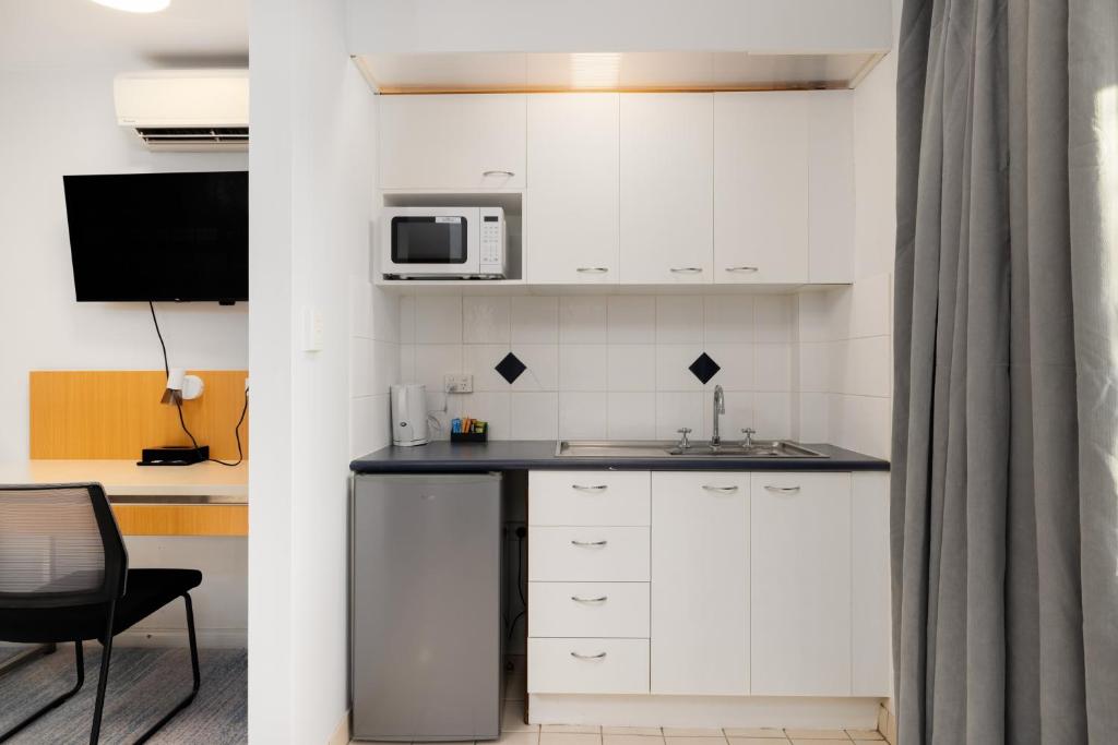 a kitchen with white cabinets and a microwave at Asraport Motel in Brisbane
