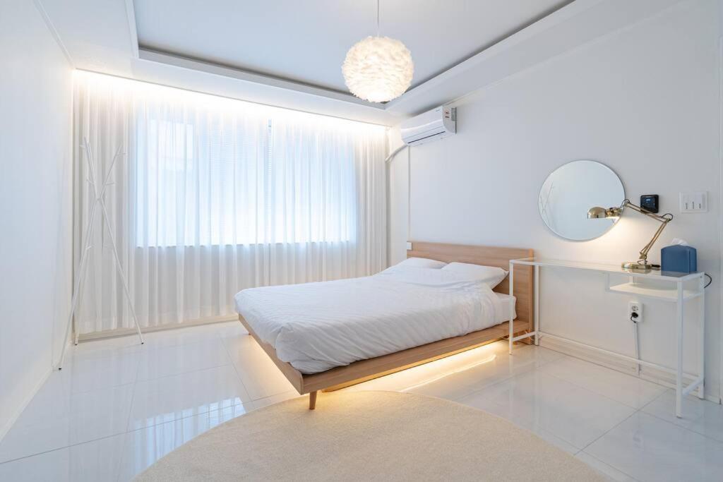 Un dormitorio blanco con una cama y un espejo. en Gangneung station chandelier house 3b, en Gangneung