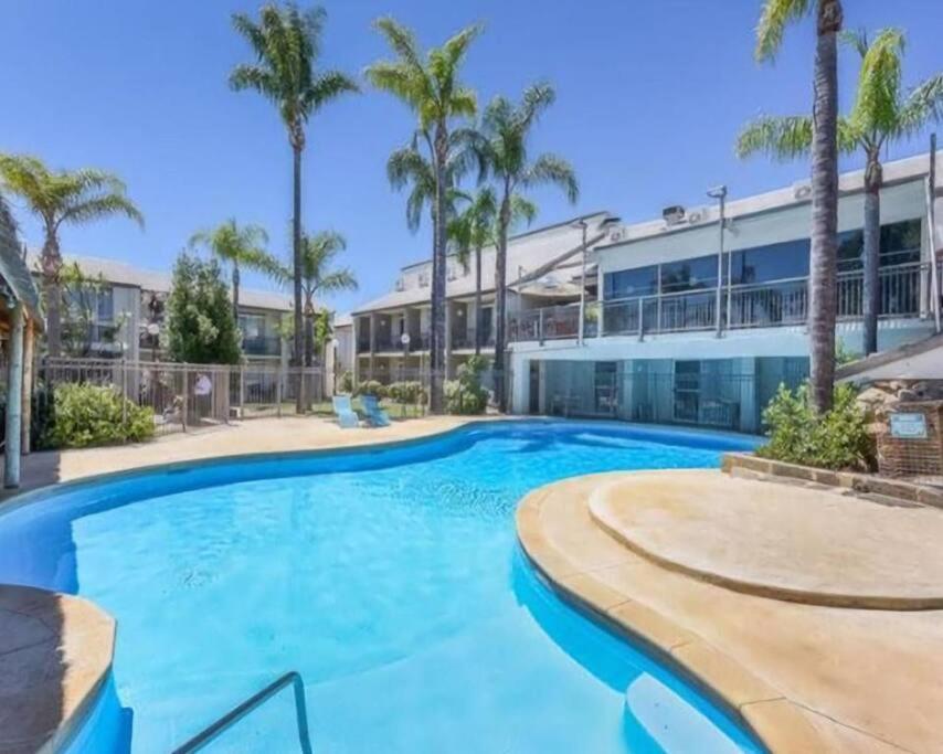 a swimming pool in front of a building with palm trees at Oasis Mandurah Resort in Mandurah