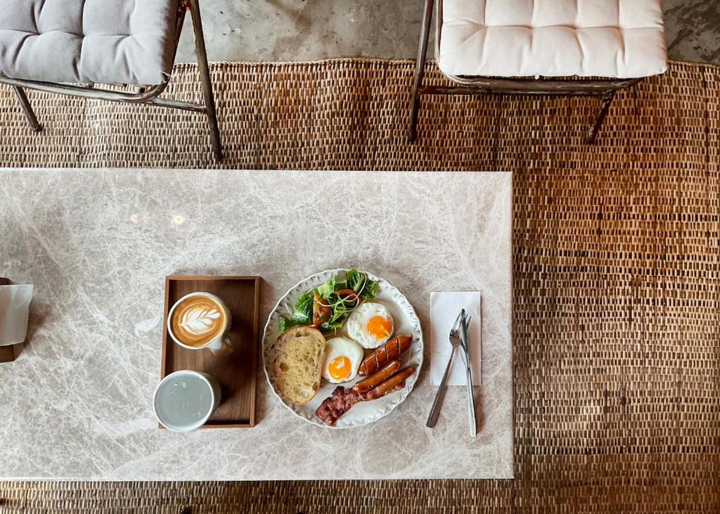 A plated breakfast of eggs, toast, sausage, greens and coffee served beside cushioned seating.