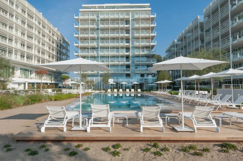 Una piscina con sillas y sombrillas frente a un edificio. en The Summer Houses Immobiliare Pacella, en Lido di Jesolo