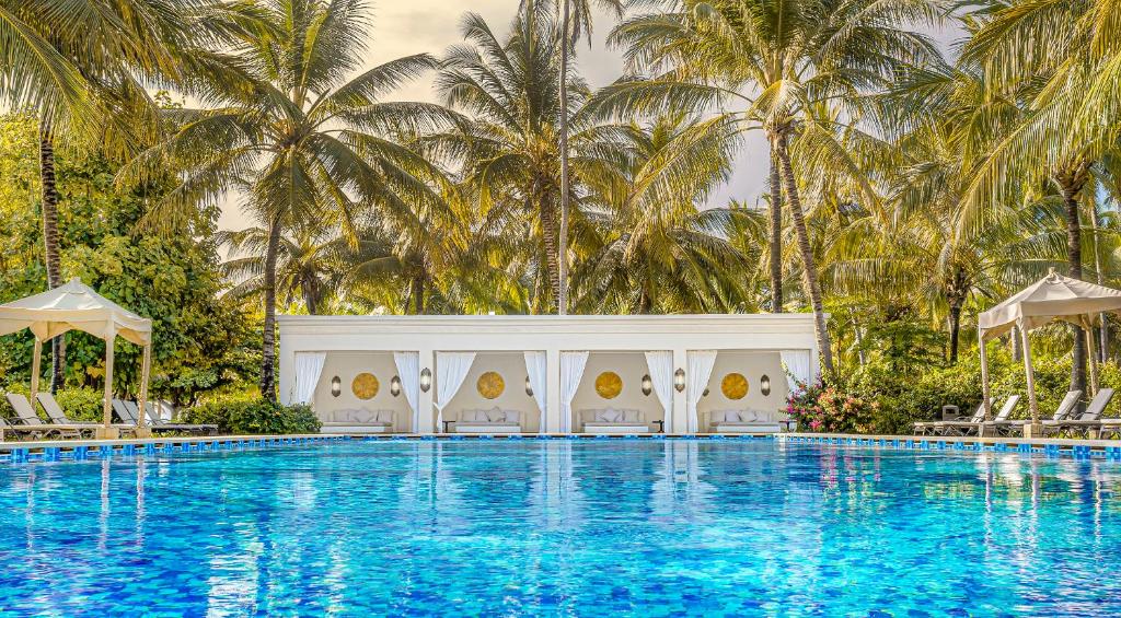 una piscina con sillas y palmeras en Baraza Resort and Spa Zanzibar, en Bwejuu